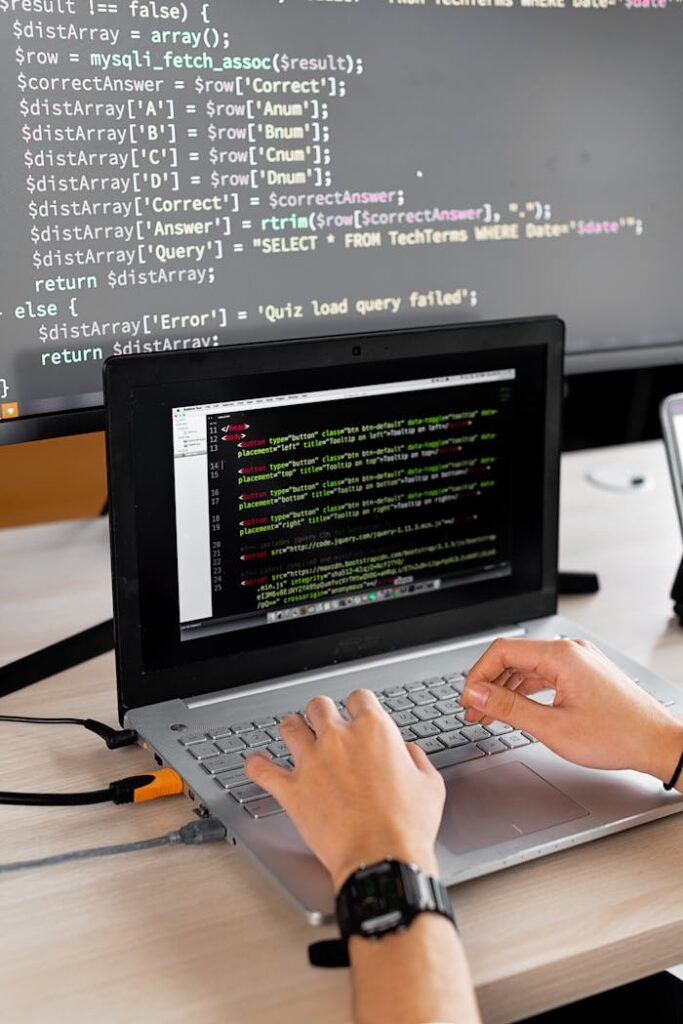 pexels photo 7988086 Person coding at a desk with laptop and external monitor showing programming code.